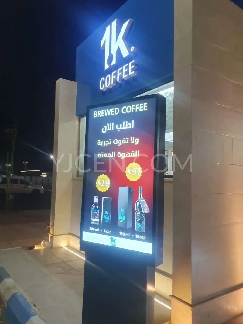 Écran vertical extérieur affichant une promotion sur le café, à côté de l’entrée d’un café, de nuit.