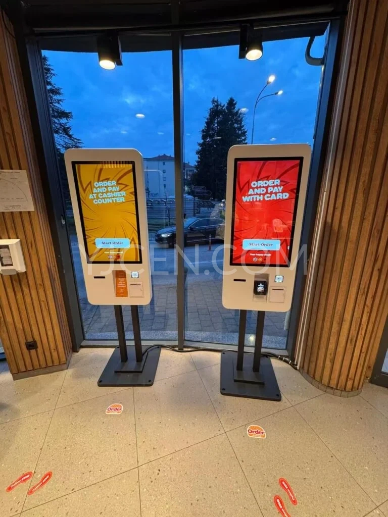 Deux bornes de commande tactiles sur pied, installées côte à côte dans un restaurant.