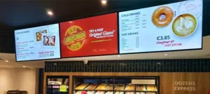 Indoor digital menu board system displaying bakery products, donuts, and hot drinks menu with pricing above service counter