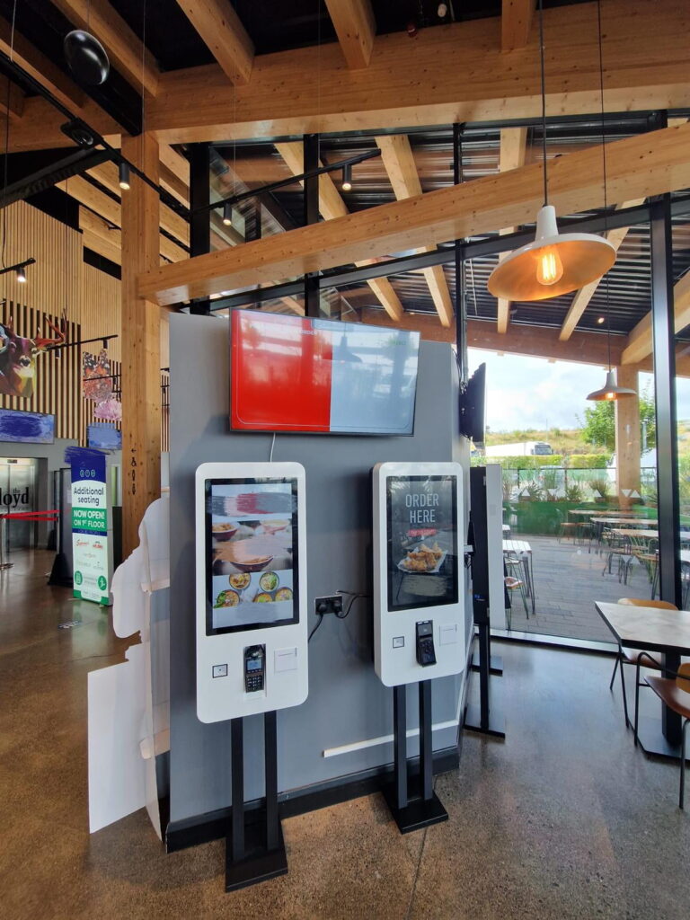 Self-service ordering kiosks with touchscreen displays and digital menu boards in modern fast food restaurant