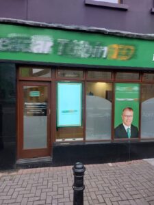 Storefront window digital signage displays showing promotional content in retail shop with green exterior frame