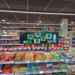 Stretch bar LCD display mounted on supermarket shelving showing fresh meal products and prepared food advertising above candy and snack aisles