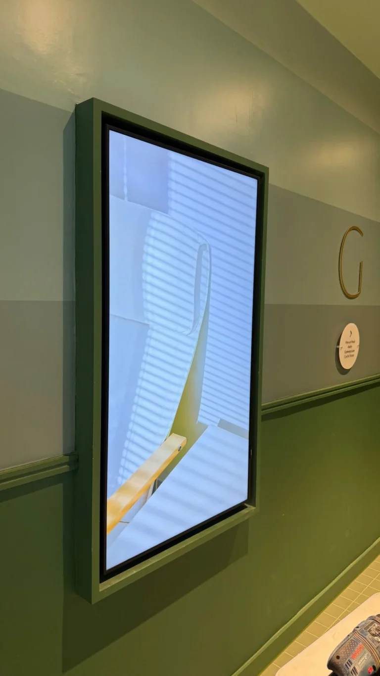 Display im Hochformat an einer grünen Wand in einem Ausstellungszentrum, mit Möbelbildern neben Hinweisschildern zu den Einrichtungen.
