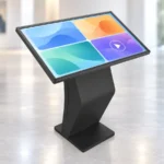 Geneigter Touchscreen im Querformat auf einer geschwungenen schwarzen Stütze mit flacher rechteckiger Bodenplatte; auf dem Bildschirm sind vier farbige Bedienkacheln zu sehen.