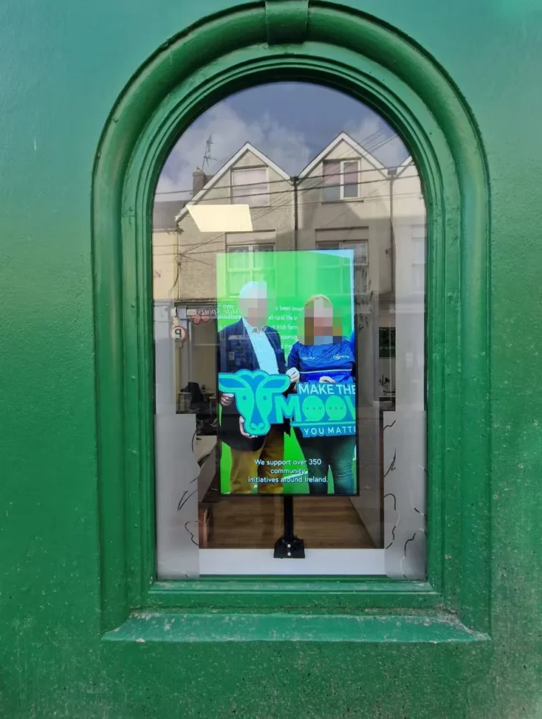Portrait display behind a green arched shop window, facing the street and showing a community support message.