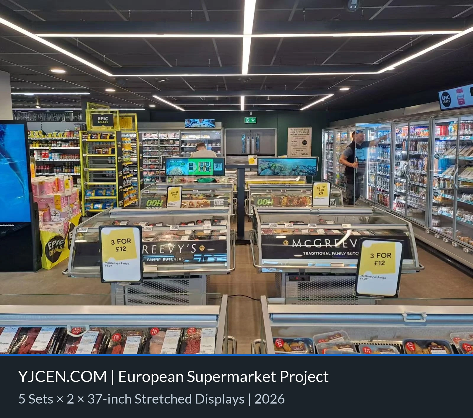 Displays em formato de barra de 37 polegadas com suportes de piso sob medida acima dos expositores refrigerados de um supermercado europeu.