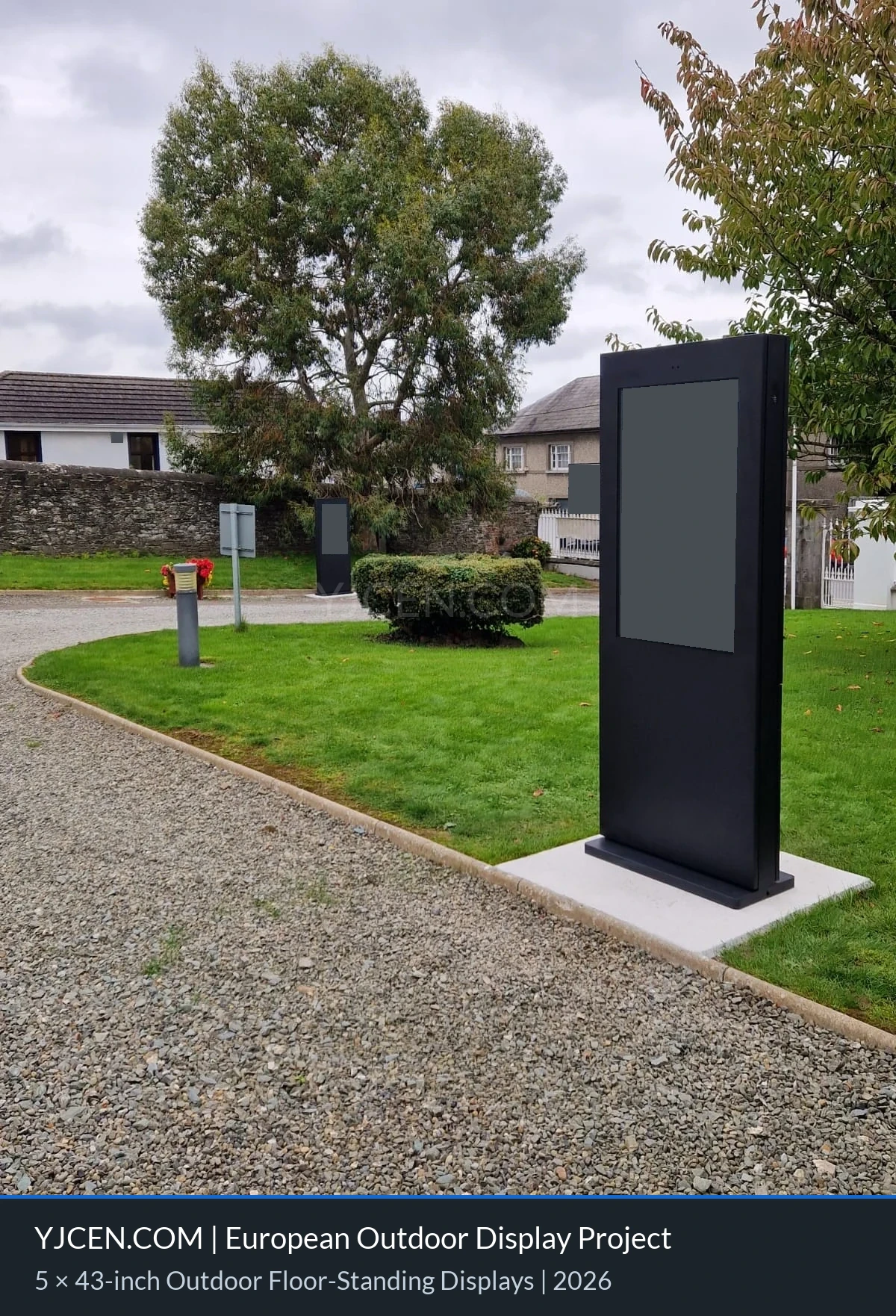 Totens digitais externos ao lado de um caminho em área ajardinada, com o conteúdo das telas e as placas ao fundo ocultados por confidencialidade.