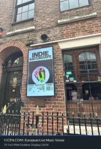 75-Zoll-IP66-Outdoor-Display im Hochformat neben dem Eingang eines europäischen Musikclubs mit Veranstaltungsmotiv.
