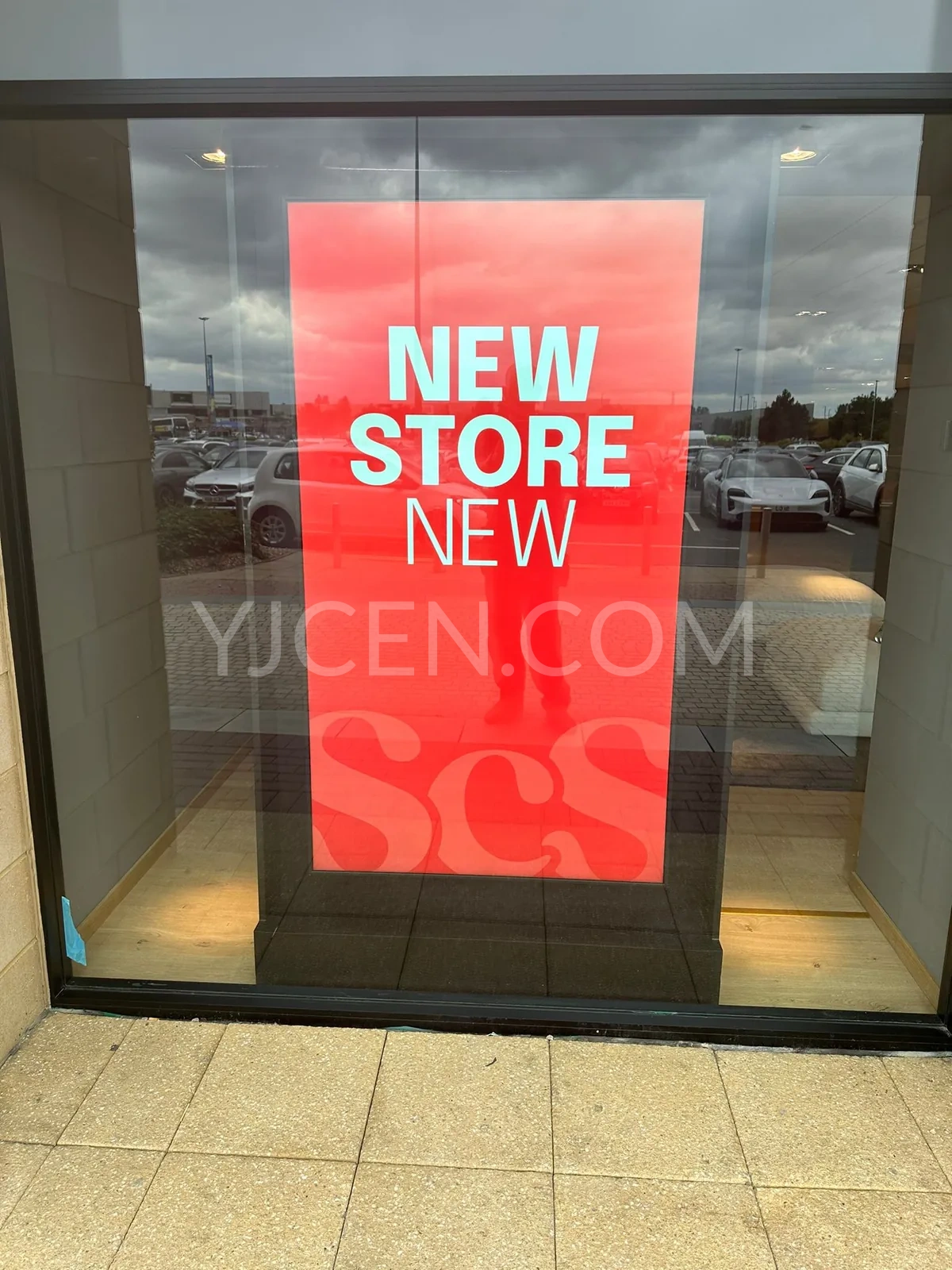 Écran YJCEN sur pied de 75 pouces annonçant un nouveau magasin derrière la vitrine.