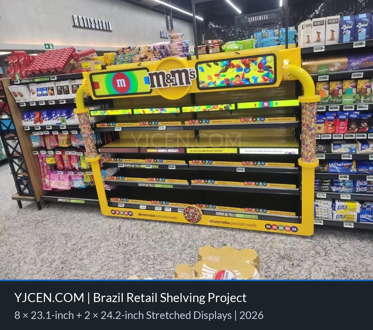 Vista d’insieme dello scaffale commerciale giallo su misura con display LCD in formato allungato tra i reparti di dolciumi di un supermercato brasiliano.