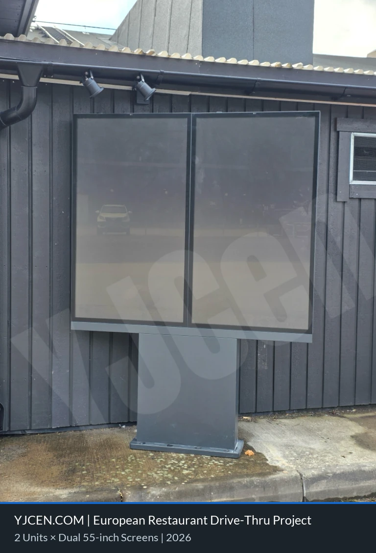 Frontansicht einer YJCEN Menütafel mit zwei ausgeschalteten 55-Zoll-Displays neben dem Restaurantgebäude.