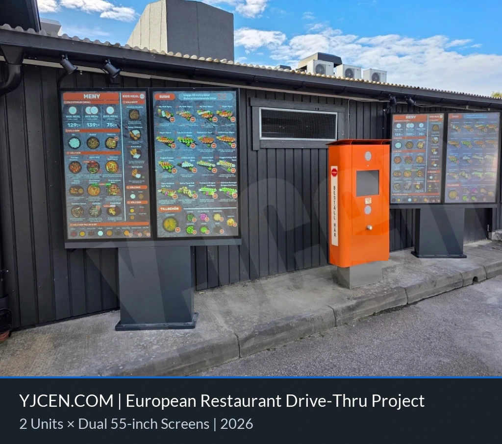 Zwei YJCEN-Doppeldisplay-Menütafeln zeigen Speisekarten neben dem Drive-thru-Bestellpunkt eines europäischen Restaurants.