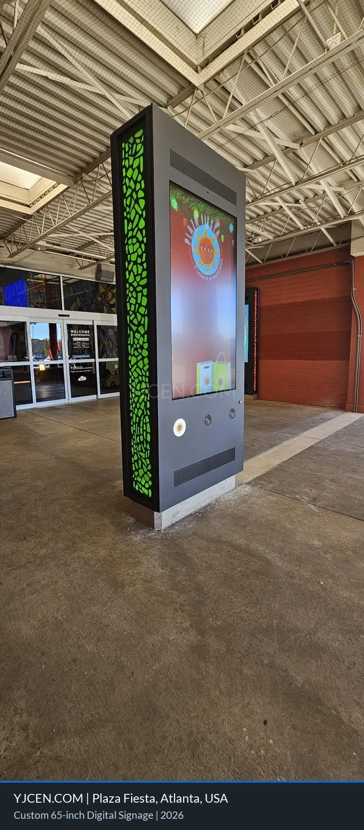Unità digital signage da 65 pollici su misura con pannelli laterali illuminati in verde all’ingresso di Plaza Fiesta.