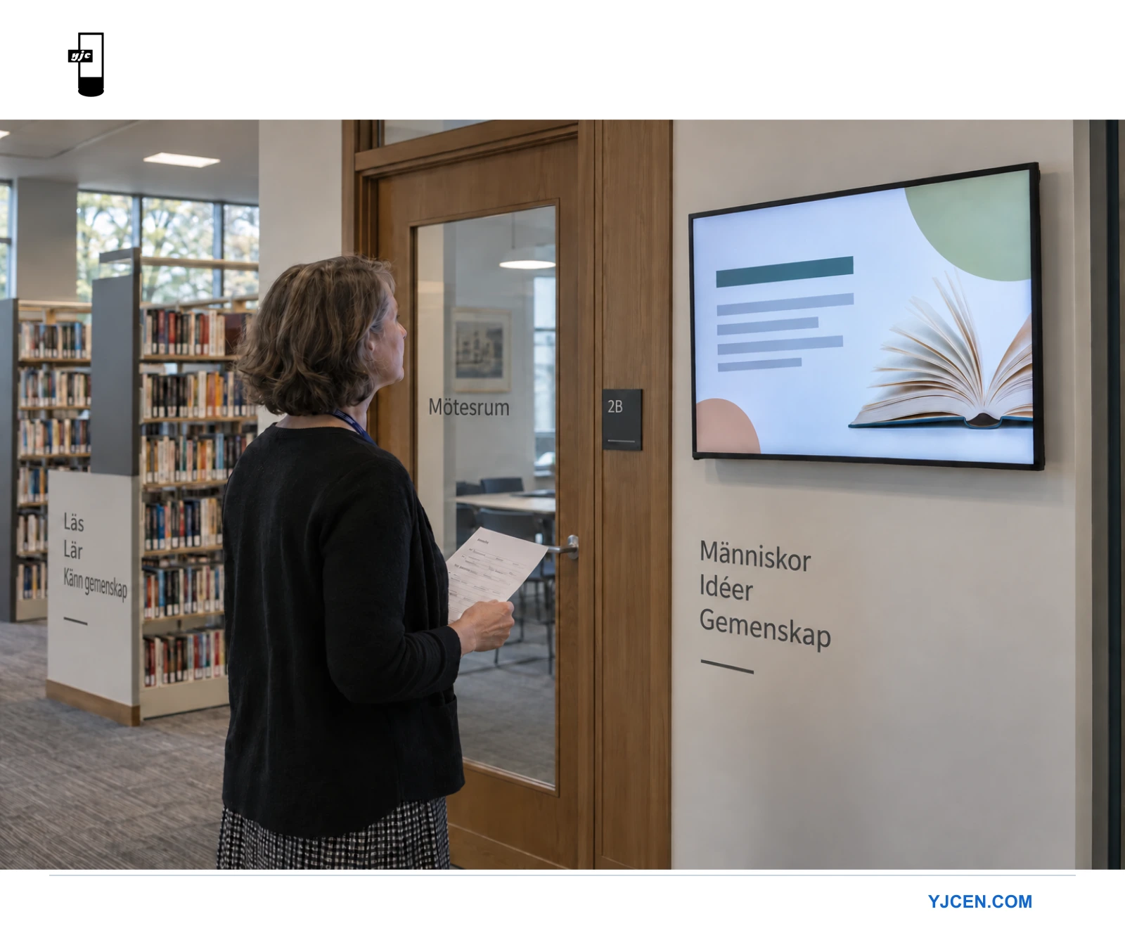 En medarbetare med checklista granskar en väggmonterad biblioteksskärm vid ingången till ett mötesrum.