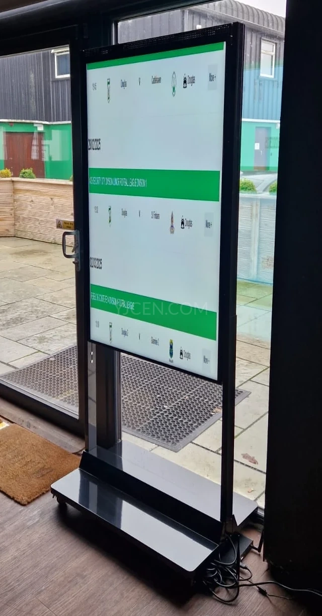 Display de vitrine vertical com uma programação em verde e branco em uma estrutura apoiada no piso ao lado de portas de vidro.